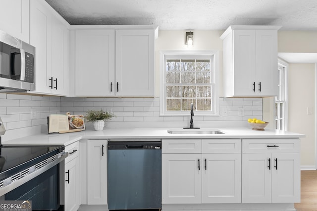 kitchen with light countertops, appliances with stainless steel finishes, a sink, and white cabinetry