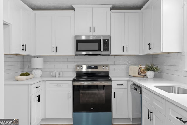 kitchen with tasteful backsplash, white cabinets, stainless steel appliances, light countertops, and a sink