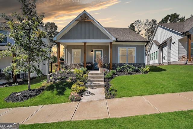 view of front of house featuring a yard, stone siding, a porch, and board and batten siding