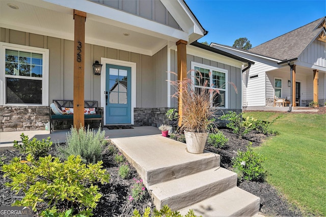 doorway to property featuring stone siding, a porch, board and batten siding, and a yard