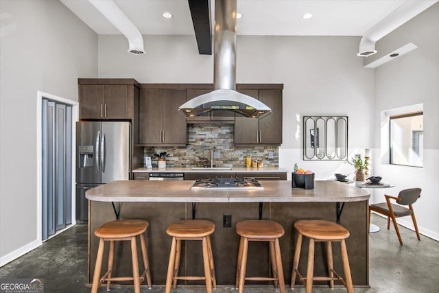 kitchen featuring island exhaust hood, finished concrete flooring, decorative backsplash, appliances with stainless steel finishes, and a sink