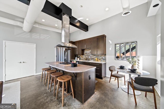 kitchen featuring dark brown cabinetry, concrete floors, light countertops, stainless steel fridge with ice dispenser, and island exhaust hood