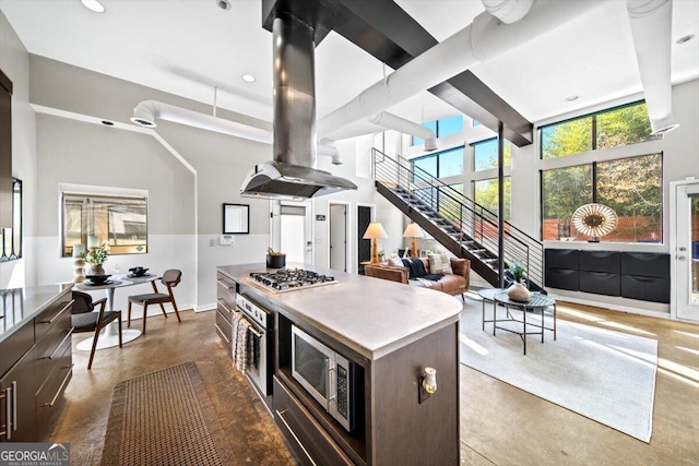 kitchen featuring a kitchen island, a towering ceiling, finished concrete flooring, appliances with stainless steel finishes, and island exhaust hood