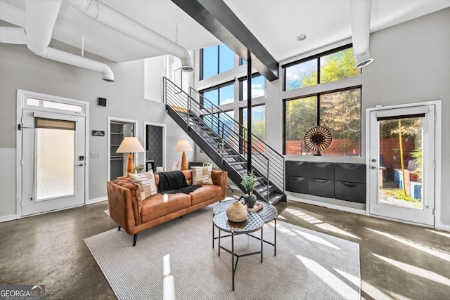 living area featuring baseboards, finished concrete flooring, a high ceiling, and stairs