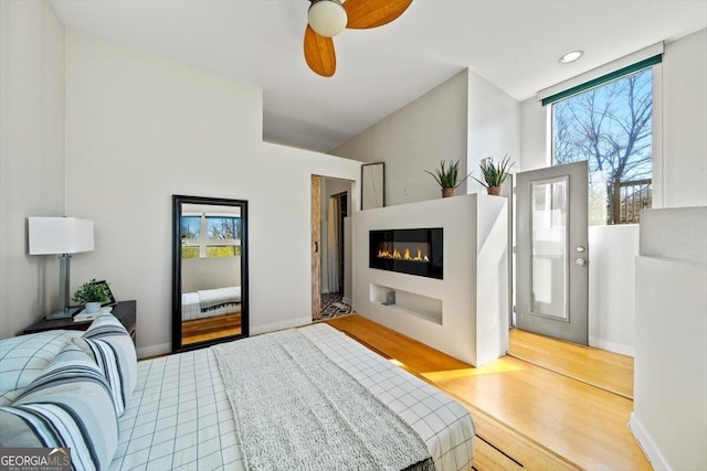 bedroom featuring a glass covered fireplace, multiple windows, ceiling fan, and wood finished floors