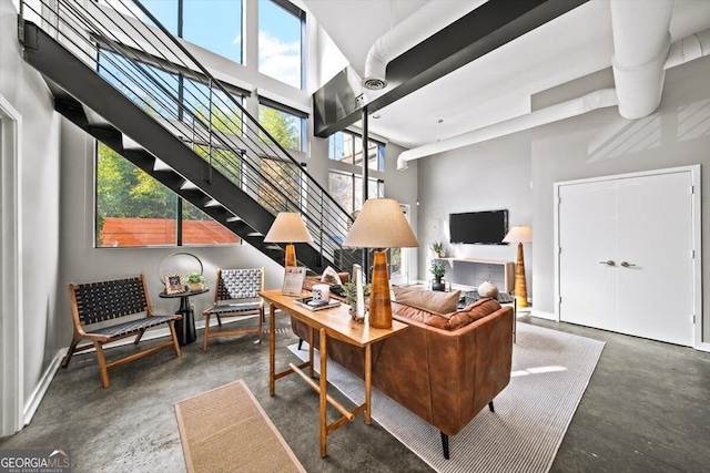 living room with concrete flooring, a towering ceiling, baseboards, and stairs