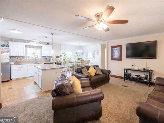 living area featuring light wood-style flooring, ornamental molding, ceiling fan, a textured ceiling, and baseboards