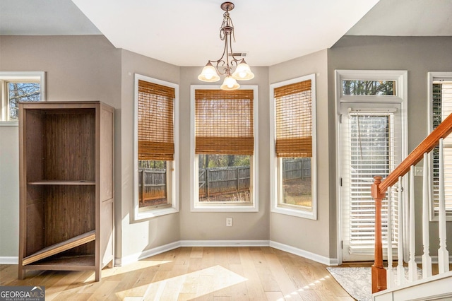 unfurnished dining area with stairs, wood-type flooring, an inviting chandelier, and baseboards