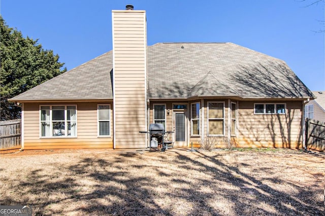 back of house featuring roof with shingles, fence, and a chimney