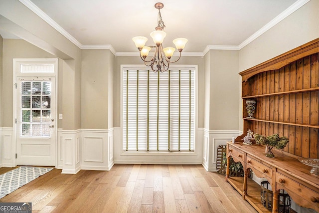 unfurnished dining area with an inviting chandelier, light wood-style flooring, ornamental molding, and wainscoting