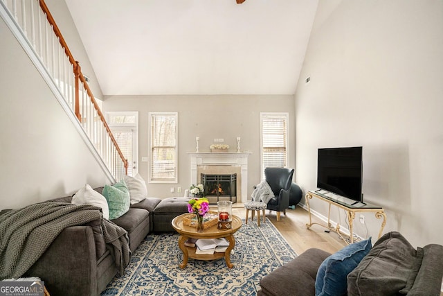 living room featuring stairs, a lit fireplace, light wood-style flooring, and a healthy amount of sunlight