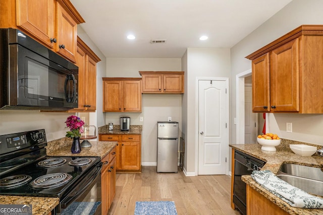 kitchen featuring black appliances, light stone counters, light wood-style flooring, and visible vents