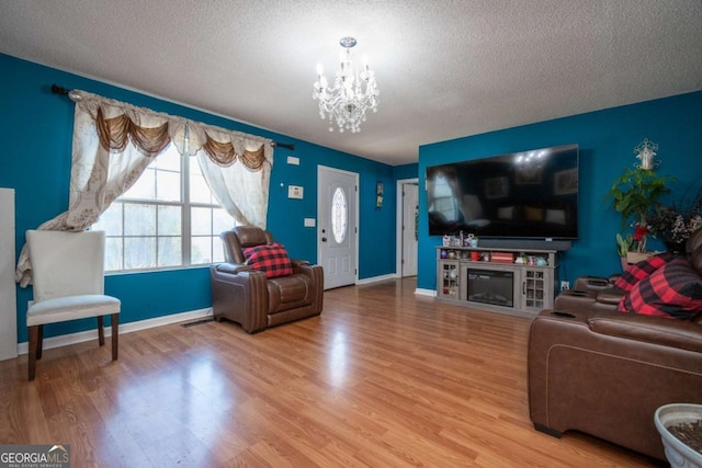 living area featuring a chandelier, a textured ceiling, wood finished floors, and baseboards