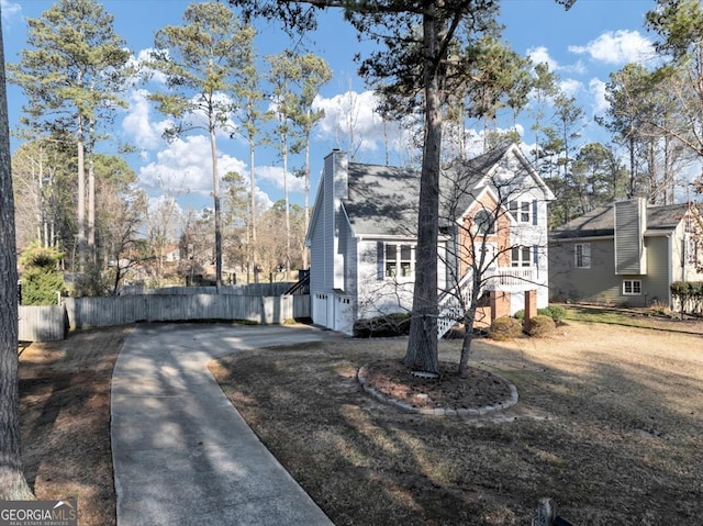 view of front facade with driveway, a chimney, and fence