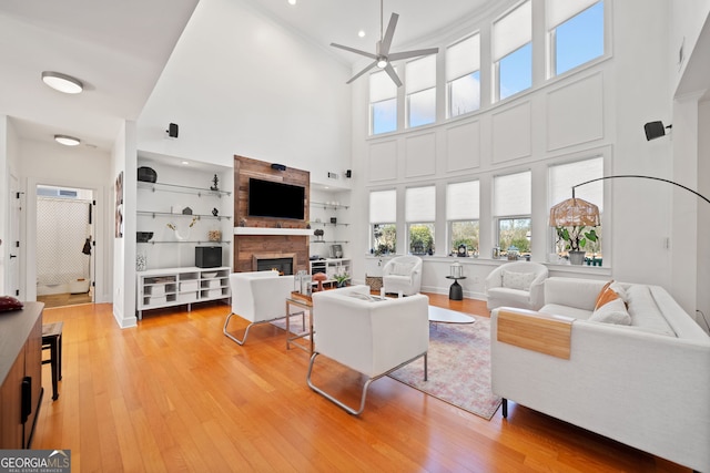 living area featuring a large fireplace, ceiling fan, and light wood-style floors