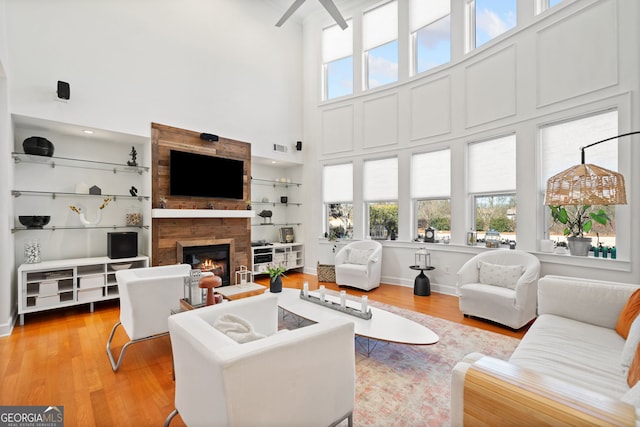 living area with a large fireplace, light wood-style flooring, a high ceiling, and visible vents