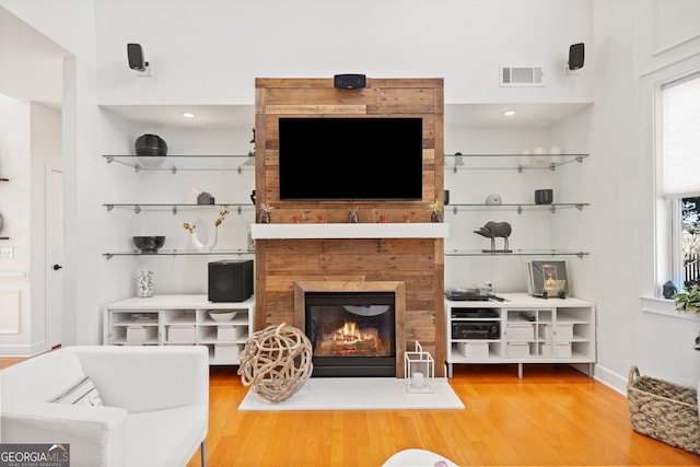 living area featuring a glass covered fireplace, visible vents, and wood finished floors