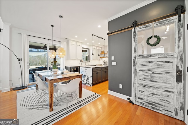 dining room featuring light wood-style floors, crown molding, baseboards, and a barn door