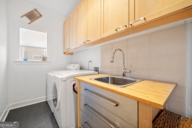 washroom with cabinet space, washing machine and dryer, a sink, dark tile patterned floors, and baseboards