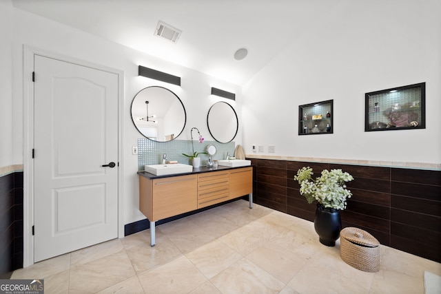 full bath featuring double vanity, visible vents, a wainscoted wall, vaulted ceiling, and a sink