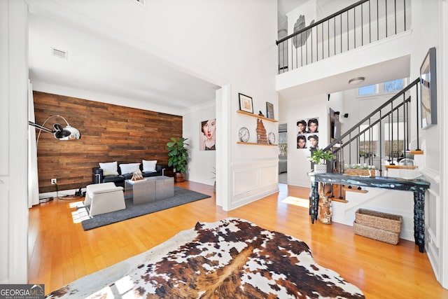 interior space featuring wooden walls, a high ceiling, wood finished floors, visible vents, and stairs