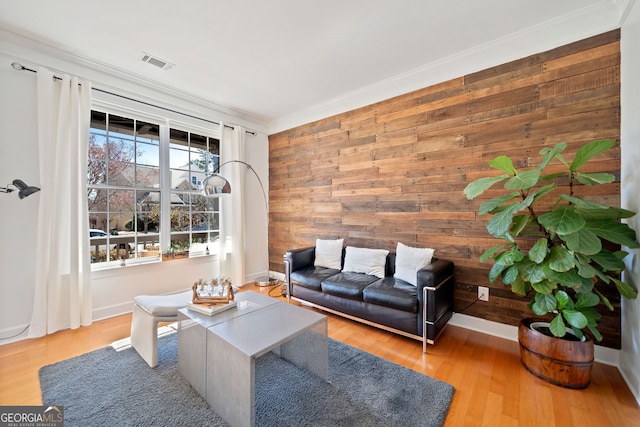 living room with crown molding, visible vents, wooden walls, wood finished floors, and baseboards