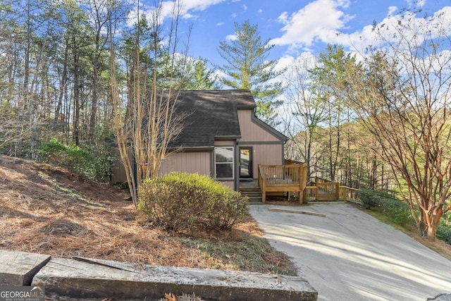 view of front of house featuring driveway, roof with shingles, and a wooden deck