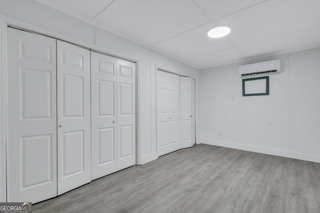 unfurnished bedroom featuring light wood-type flooring, a wall mounted air conditioner, baseboards, and two closets