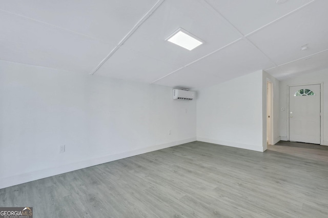 spare room featuring lofted ceiling, baseboards, wood finished floors, and a wall mounted AC