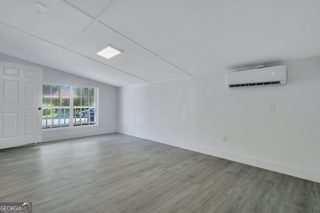 empty room featuring baseboards, vaulted ceiling, an AC wall unit, and wood finished floors