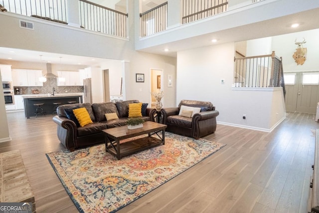 living area featuring a high ceiling, visible vents, baseboards, stairs, and light wood finished floors