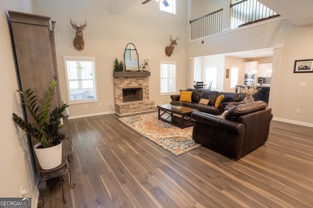 living room featuring baseboards, a ceiling fan, a towering ceiling, dark wood-type flooring, and a fireplace
