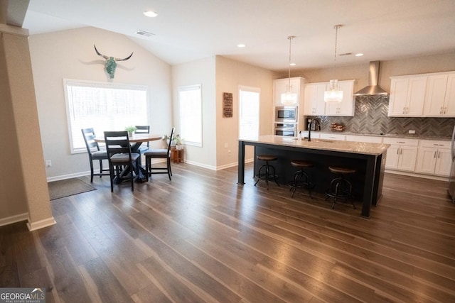 kitchen featuring dark wood-style floors, decorative backsplash, appliances with stainless steel finishes, a sink, and wall chimney exhaust hood