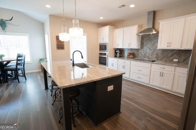 kitchen with visible vents, appliances with stainless steel finishes, a sink, an island with sink, and wall chimney exhaust hood
