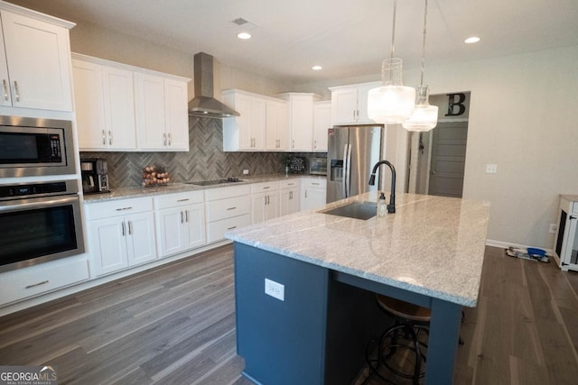 kitchen with white cabinets, wall chimney exhaust hood, appliances with stainless steel finishes, dark wood-style flooring, and a sink