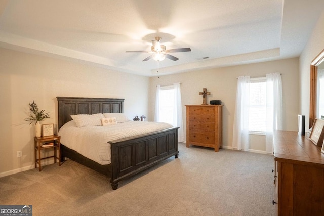bedroom with a tray ceiling, light carpet, and multiple windows