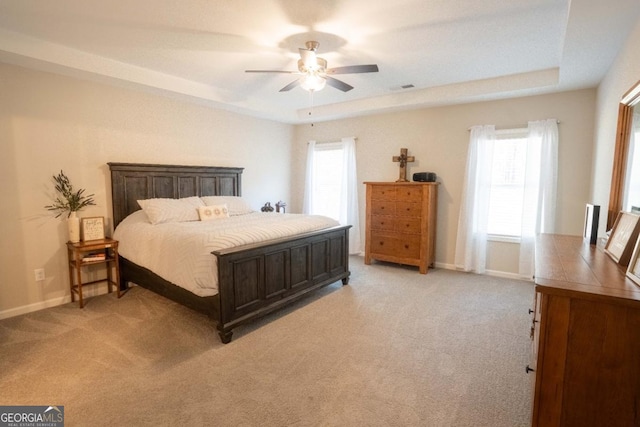 bedroom featuring baseboards, visible vents, a ceiling fan, light colored carpet, and a tray ceiling
