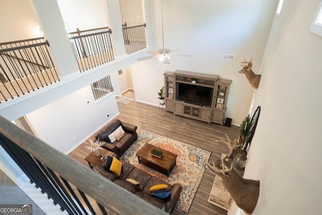 living area with baseboards, a towering ceiling, ceiling fan, wood finished floors, and stairs