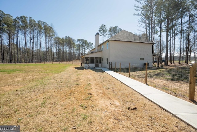exterior space with a sunroom, a chimney, fence, and a lawn