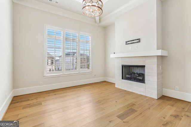 unfurnished living room featuring a tile fireplace, a notable chandelier, visible vents, baseboards, and hardwood / wood-style floors