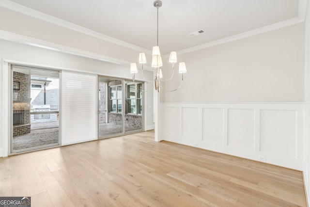 unfurnished dining area featuring a chandelier, light wood-style flooring, visible vents, wainscoting, and crown molding