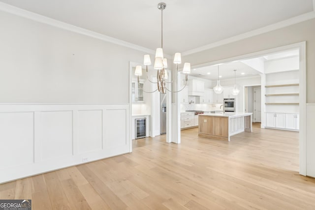 unfurnished dining area featuring a wainscoted wall, light wood-style flooring, wine cooler, and ornamental molding