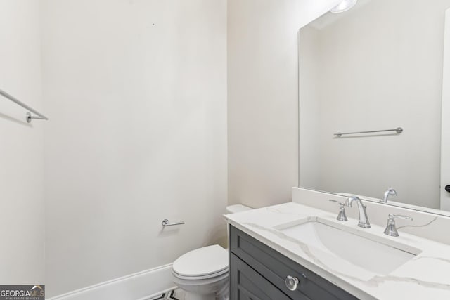 half bathroom featuring toilet, baseboards, and vanity