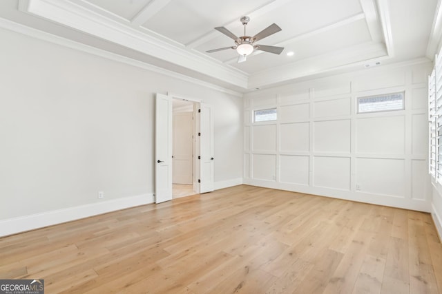 spare room with ceiling fan, light wood-style flooring, ornamental molding, a tray ceiling, and a decorative wall