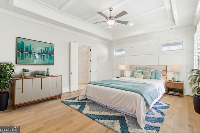 bedroom with ceiling fan, a decorative wall, light wood-style floors, ornamental molding, and a tray ceiling