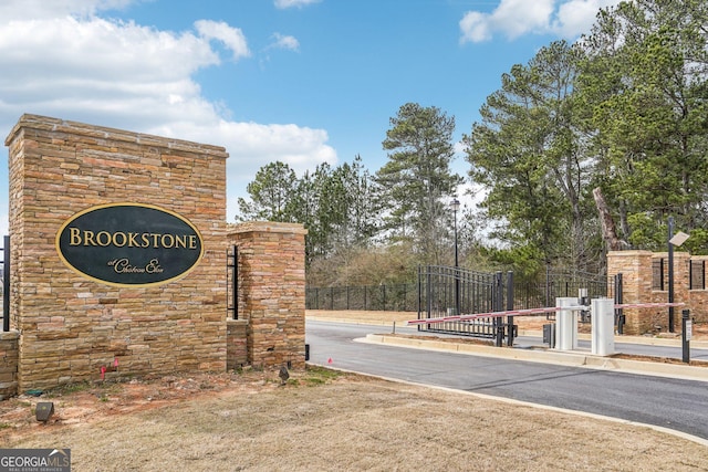 community / neighborhood sign featuring fence and a gate