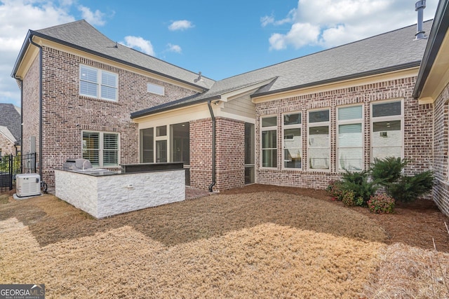 back of house featuring brick siding, area for grilling, a sunroom, and a shingled roof