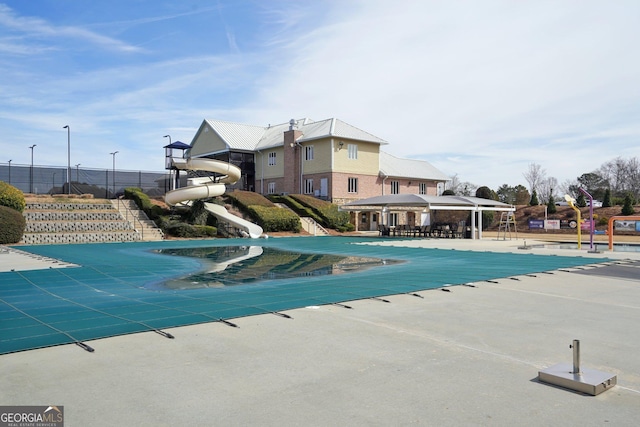 community pool with a patio area, fence, a water slide, and a gazebo