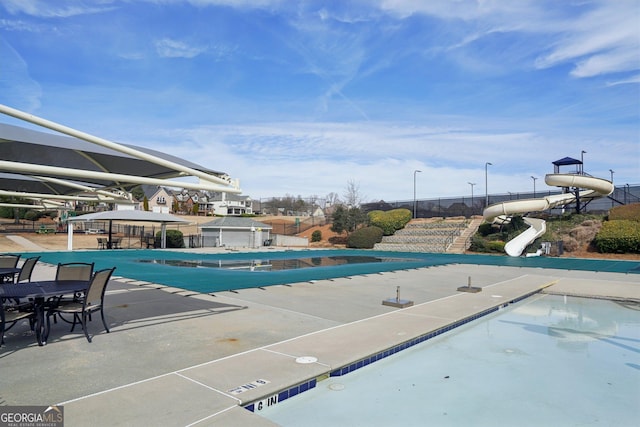 community pool with a water slide, a patio area, and fence