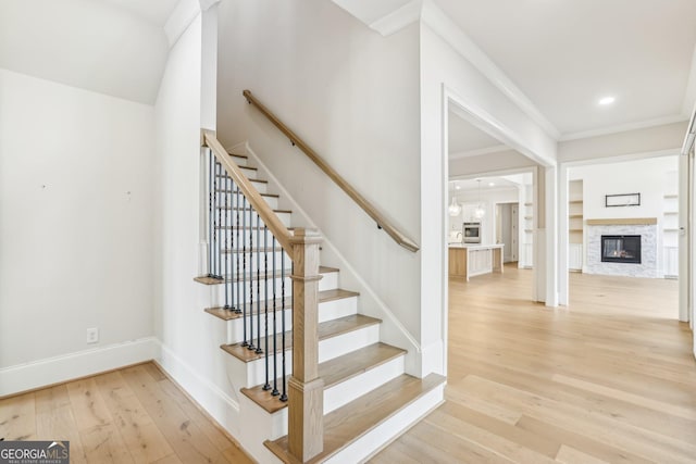 staircase with baseboards, a glass covered fireplace, hardwood / wood-style flooring, ornamental molding, and recessed lighting